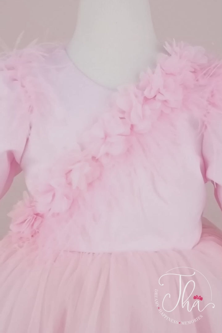 360° view of a pink designer dress that has 3D flowers, long sleeves, feathers, shirring detail, V design, bow, and knee length skirt
