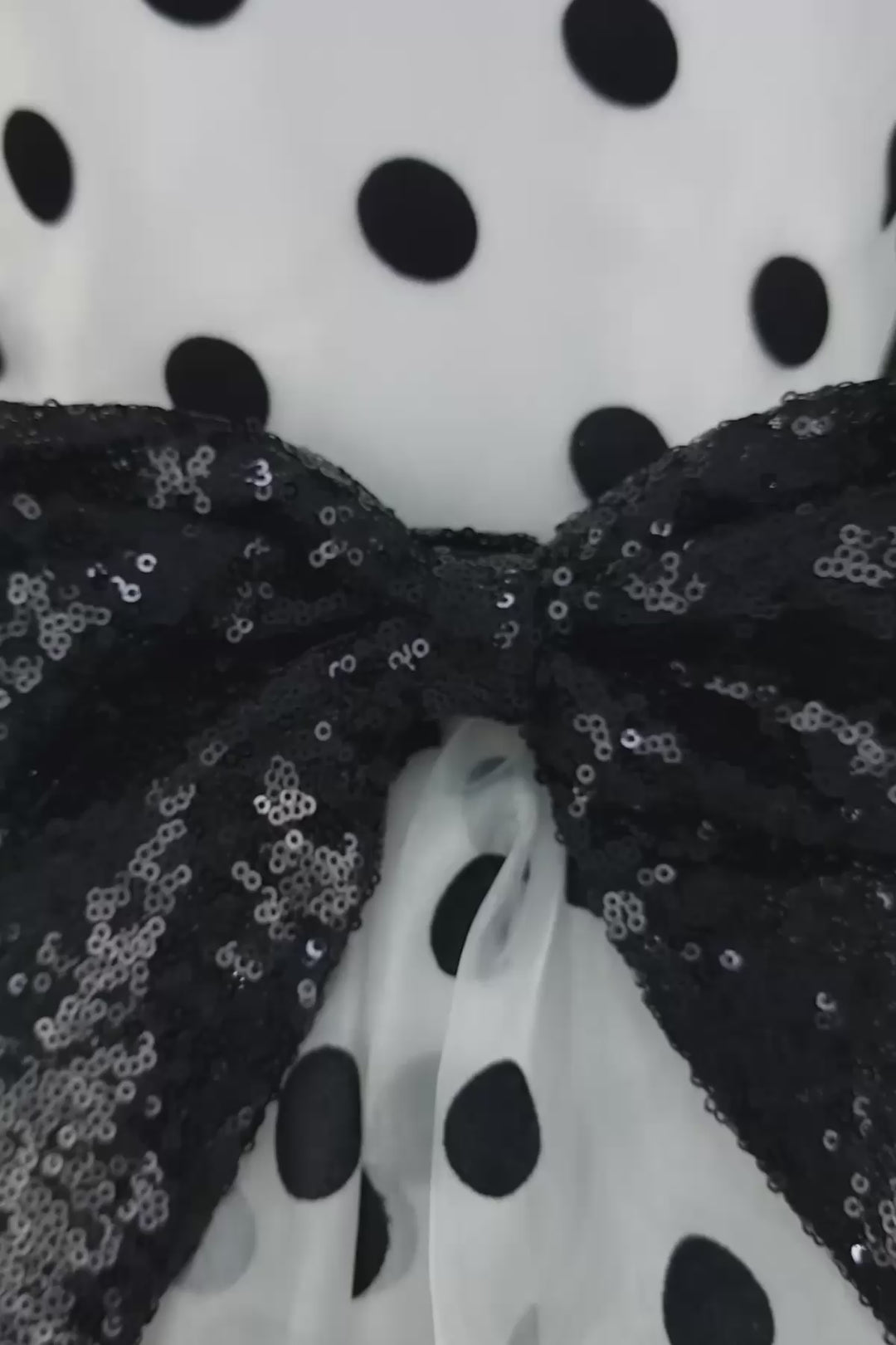 360° view of a white elegant sleeveless dress that has black polka dots, judge collar, tulle ruffle and black sequin bow ribbon