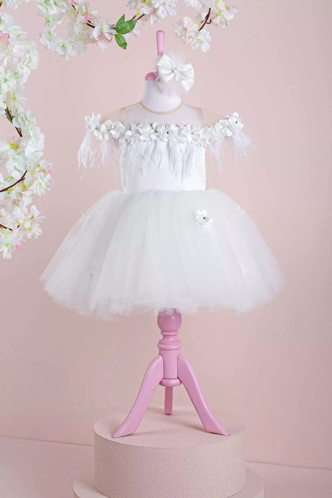 A white sleeveless bridesmaid dress that has 3D flowers with rhinestones, cap sleeve, feathers, illusion collar, satin top, and knee length skirt