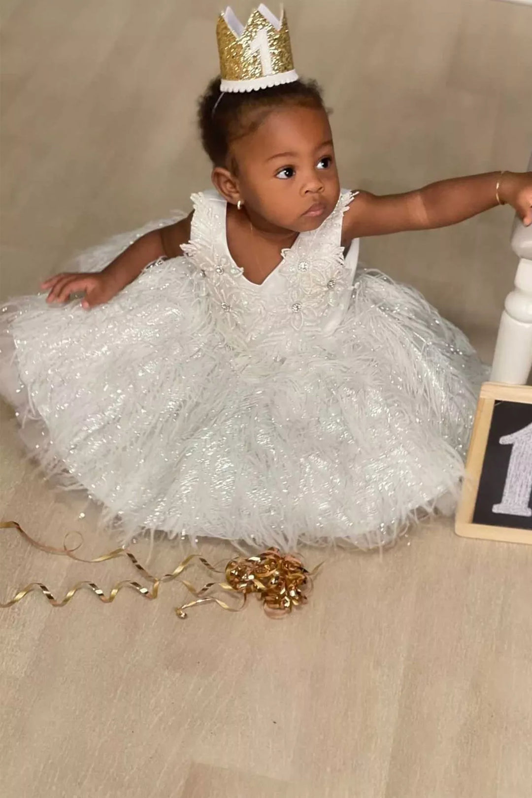 Baby girl in a white flower dress and gold crown at her first birthday photo shoot
