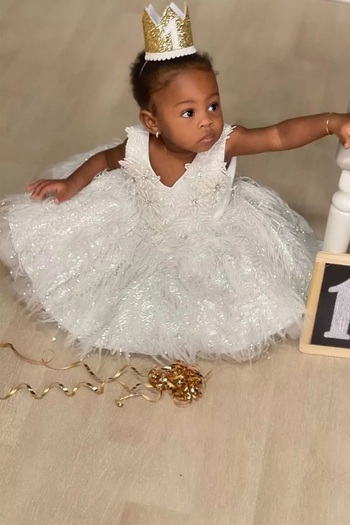 Baby girl in a white flower dress and gold crown at her first birthday photo shoot