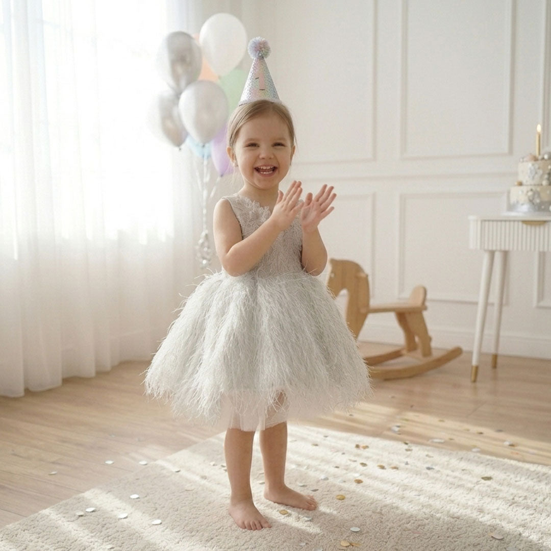 Toddler girl in a white lace birthday dress clapping at her birthday party