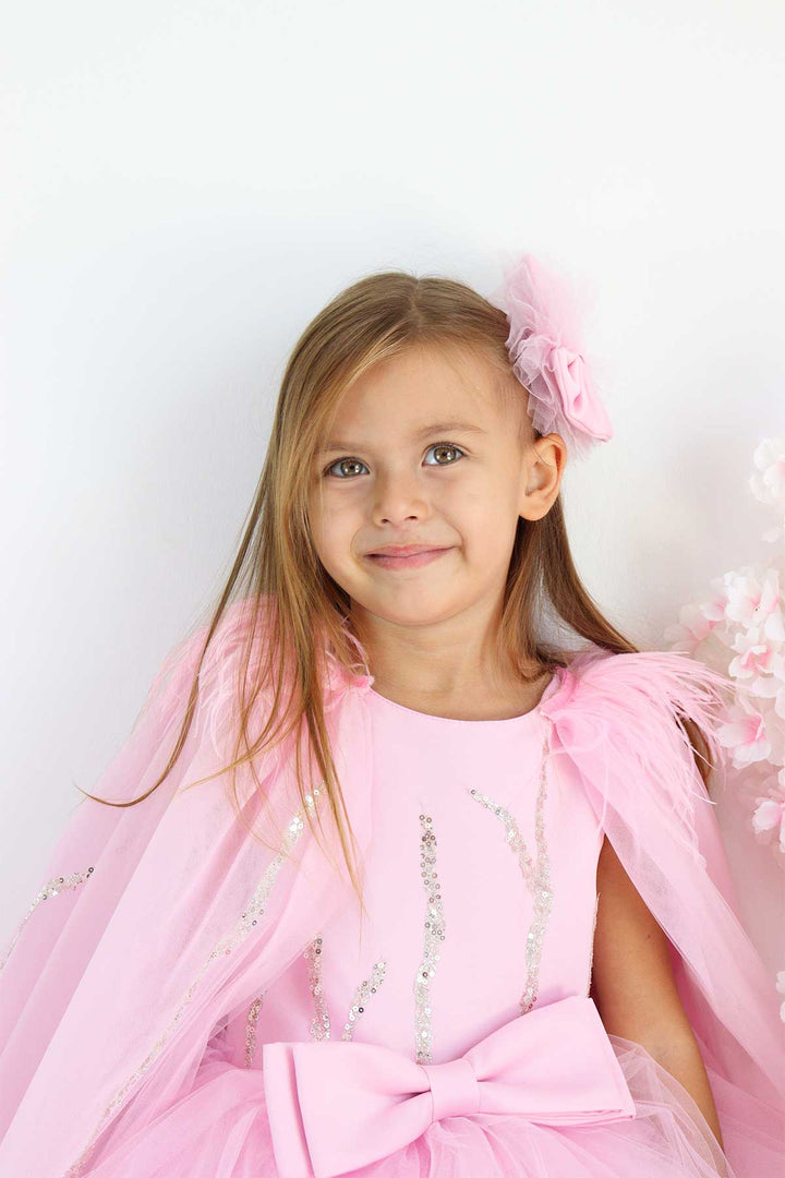Close up view of a pink birthday party dress. The dress has a knee length skirt, cape, and a pink bow at the waist. The skirt is made of layers of pink tulle