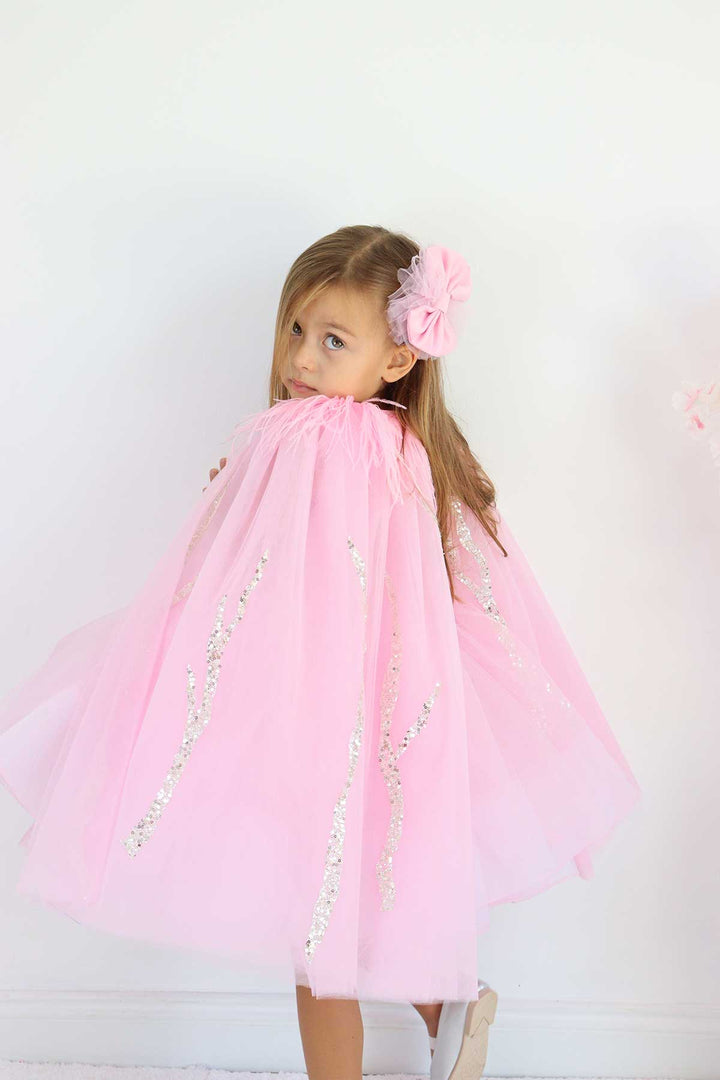 A pink birthday party dress. The dress has a knee length skirt, cape, and a pink bow at the waist. The skirt is made of layers of pink tulle