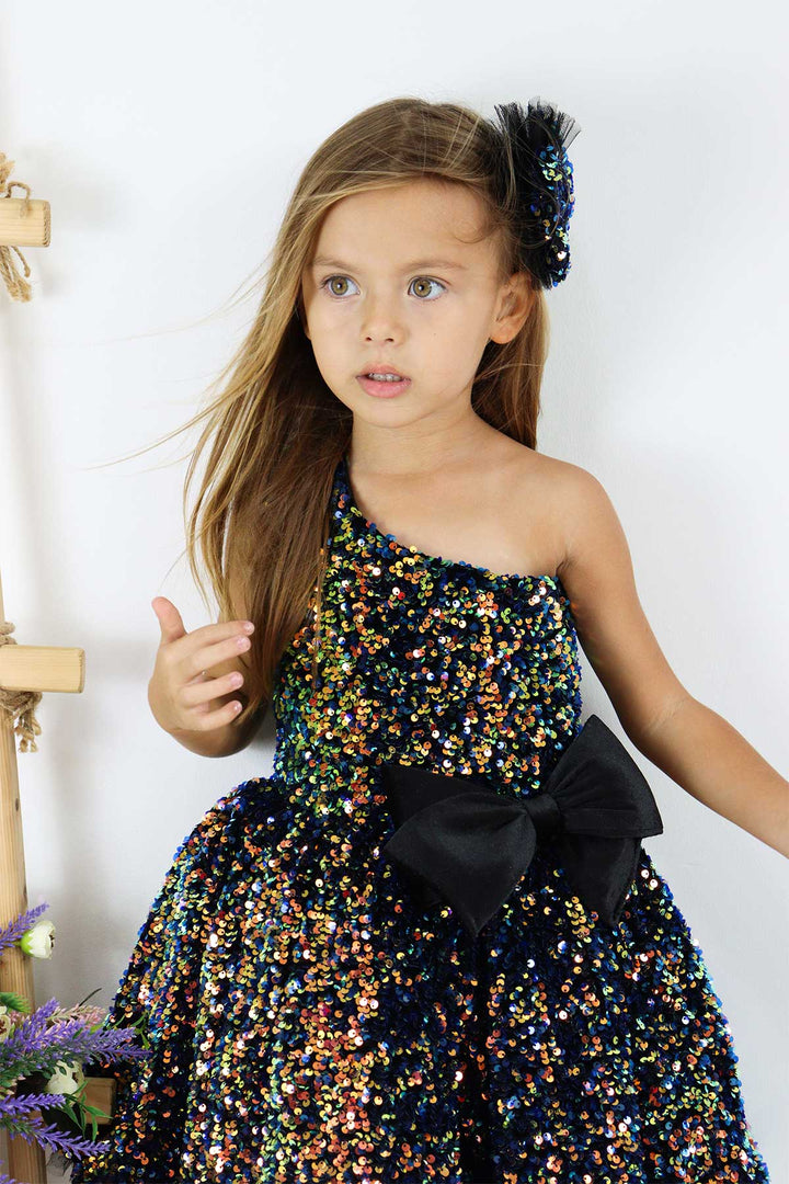 Close up view of a black hologram sequin one shoulder open Christmas dress that has velvet ribbon and knee length skirt