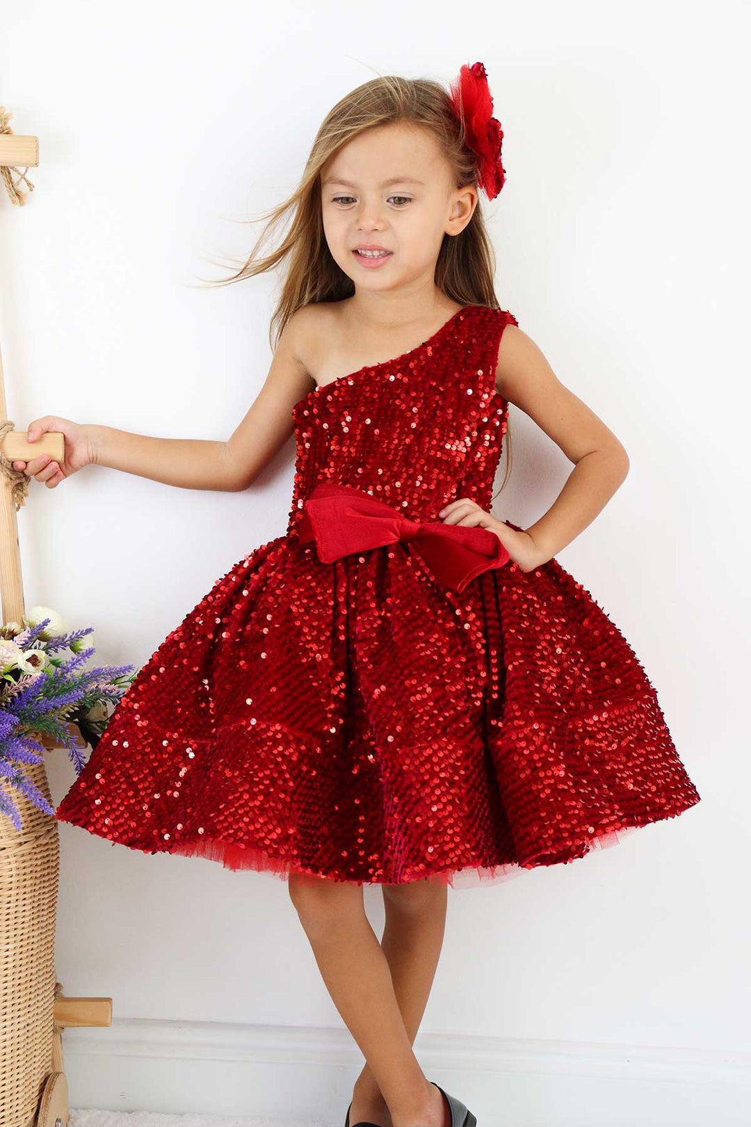 Close up view of a red hologram sequin one shoulder open Christmas dress that has velvet ribbon and knee length skirt