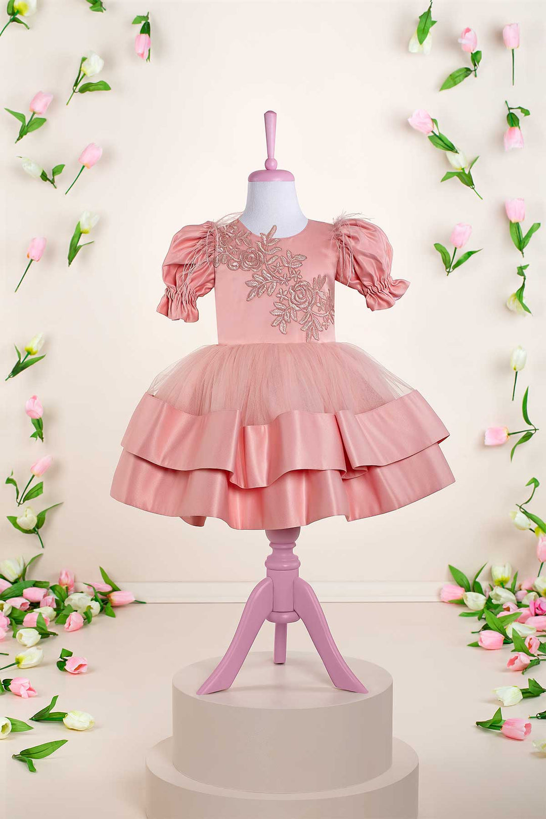 A pink baby dress that has balloon arm, half sleeves, lace embroidery, dream tulle knee length skirt, and feathers