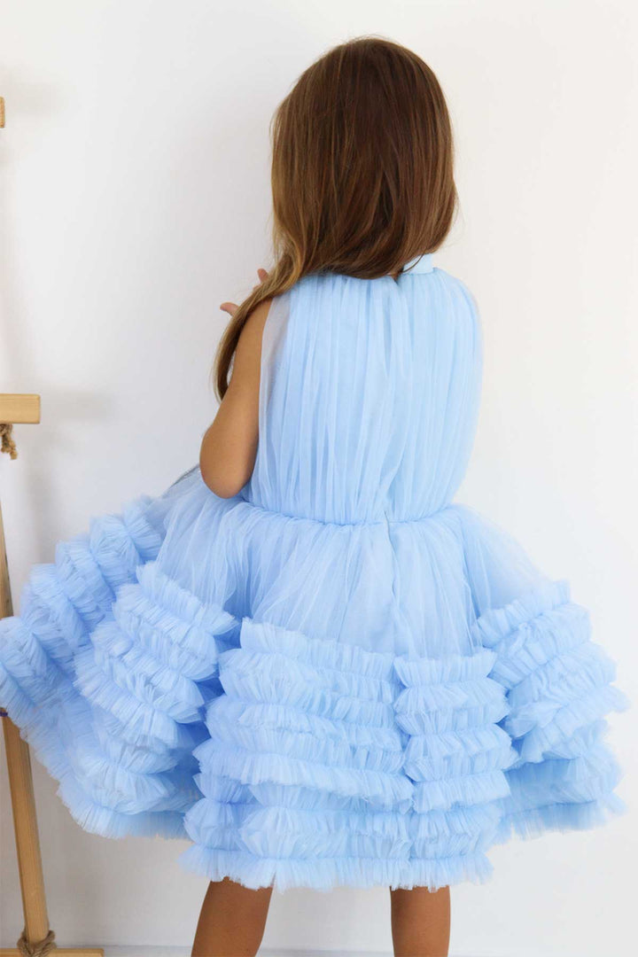 Back view of a blue sleeveless elegant dress that has judge collar, tulle top, shirred tulle knee length skirt