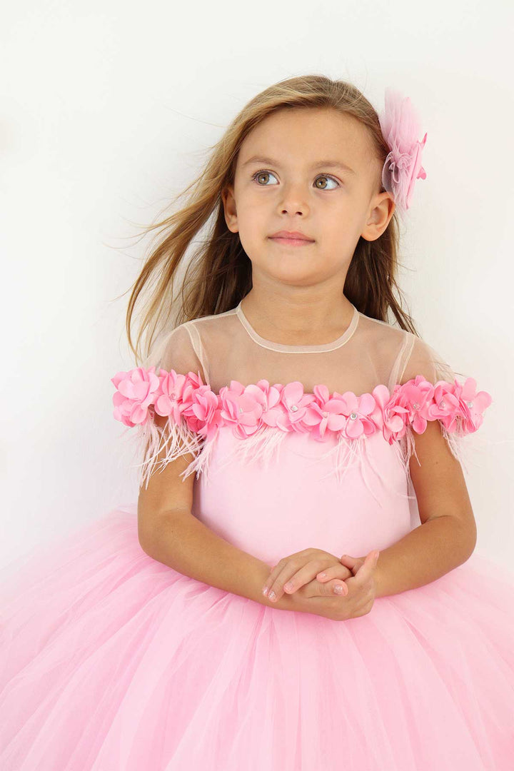 Close up view of a pink sleeveless fairy dress that has 3D flowers with rhinestones, cap sleeve, feathers, illusion collar, knee length skirt, and satin top