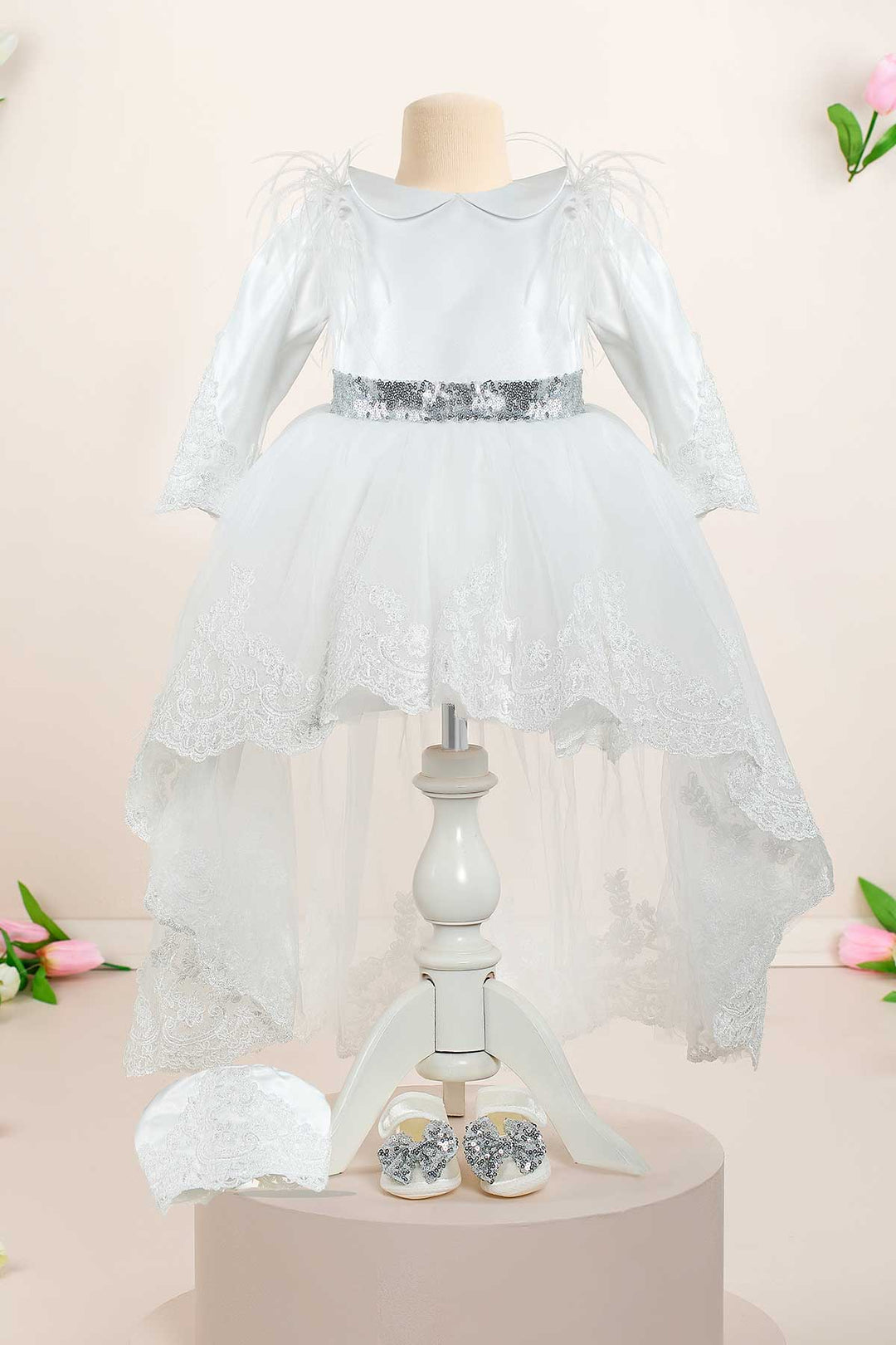 A white baptism dress set that has long sleeves, feathers, baby collar, hood, shoes, headband, silver sequin belt, long train, and lace on sleeves and hems