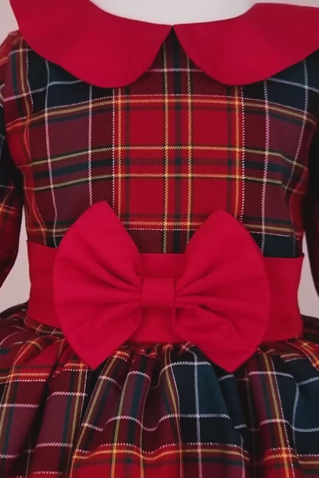 360° view of a red plaid Christmas dress that has long sleeves, baby collar, bow, belt, and knee length skirt