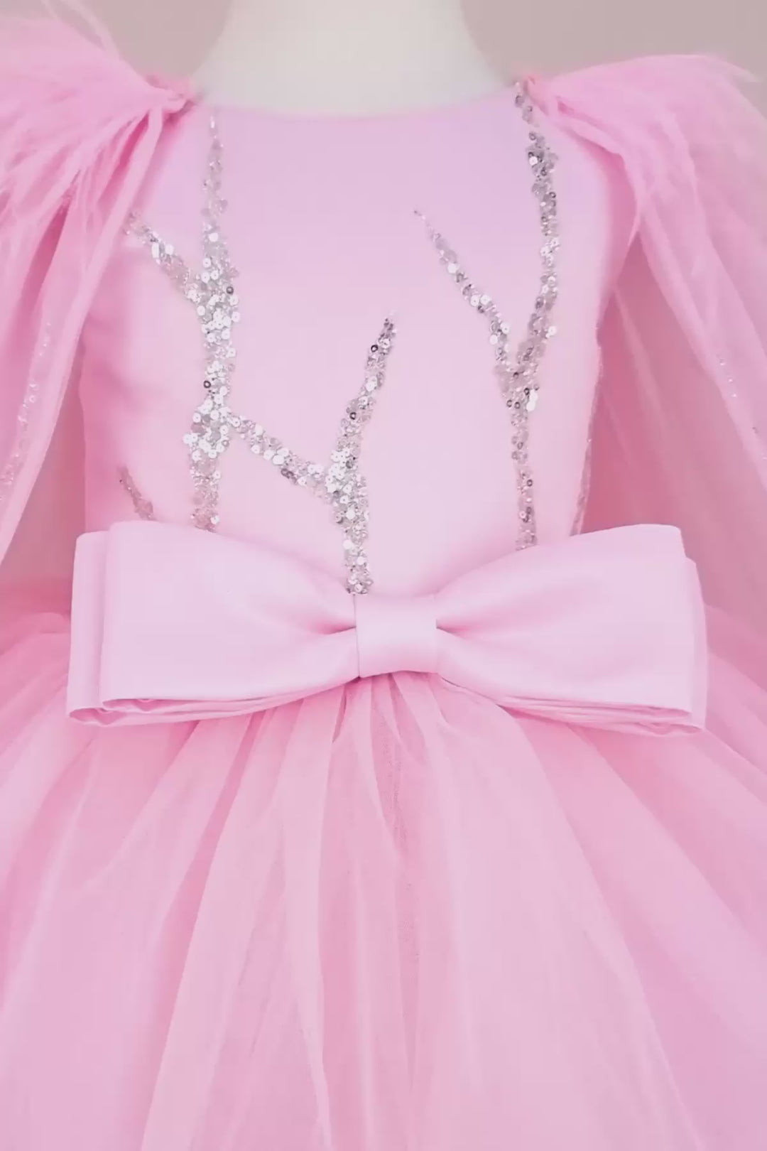 360° view of a pink birthday party dress. The dress has a knee length skirt, cape, and a pink bow at the waist. The skirt is made of layers of pink tulle