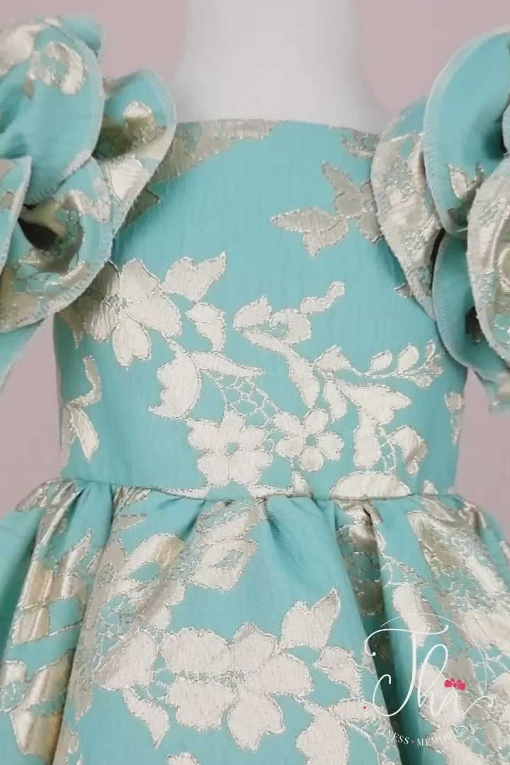 360° view of a mint green Easter dress that has brocade fabric, 3D floral gold print, 3D flowers on shoulders, boat collar, and knee length skirt