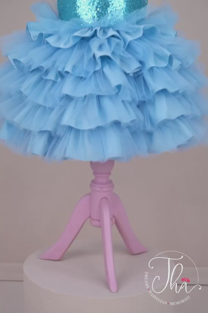 360° view of a blue ice concept dress that has balloon arm, feathers, blue sequin top and bow, and tulle and satin knee length skirt