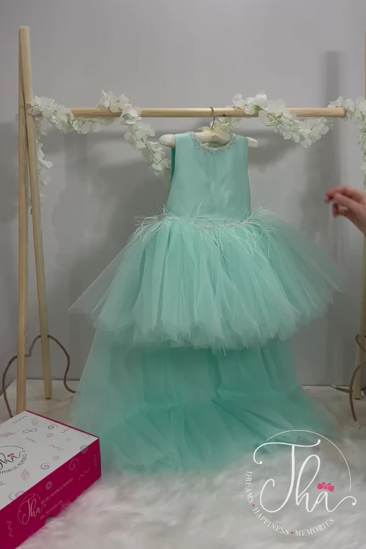 360° view of a mint green sleeveless princess dress that has hi-low skirt, pearl belt and collar, feathers, V design, and bow