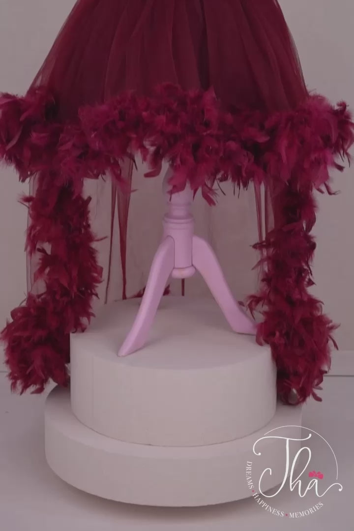 360° view of a burgundy princess dress that has cap sleeves, feathers on shoulders and hems, hi-low skirt, V design, and burgundy sequin top and bow