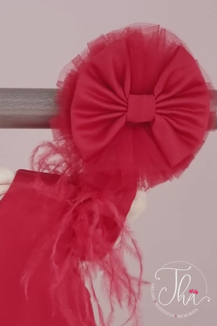 360° view of a red baby dress that has cap sleeves, feathers, satin top, bow, tulle, and satin knee length skirt