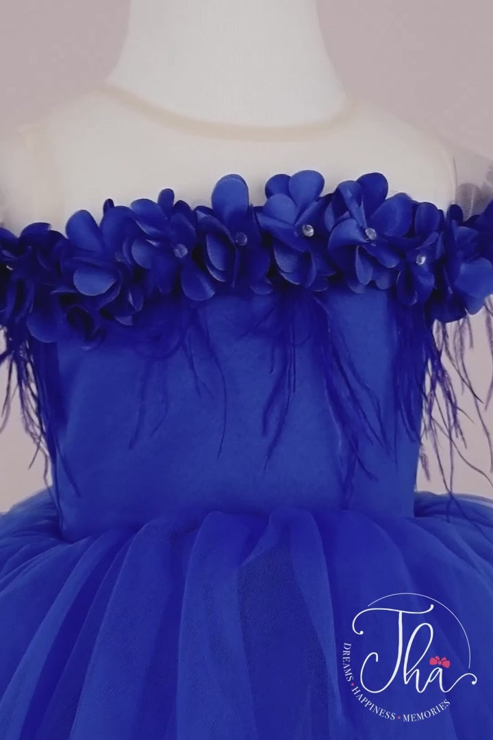 360° view of a sax blue sleeveless Snow Queen dress that has 3D flowers with rhinestones, cap sleeve, feathers, illusion collar, satin top, and knee length skirt