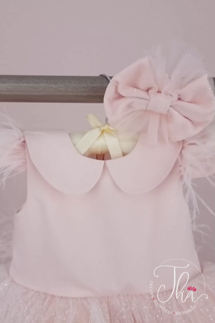 360° view of a pink baby dress that has cap sleeves, feathers, bow, baby collar, lace on hems, and tulle knee length skirt