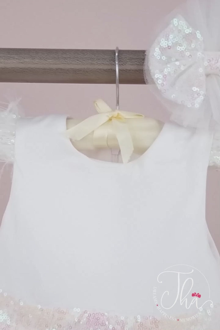 360° view of a white christening dress that has white sequin cap sleeves, feathers, sequin belt and bow, and knee length skirt