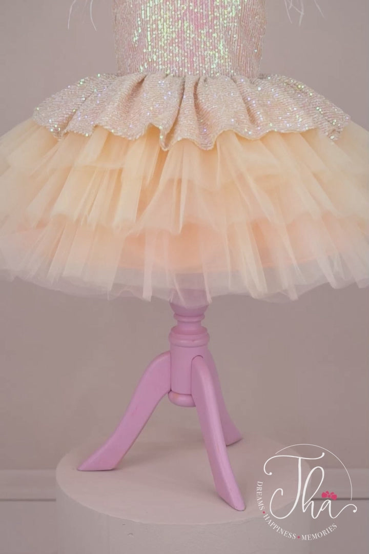 360° view of a powder candy concept dress that has cap sleeves, powder sequin top and bow, feathers, V design, and knee length tulle layered skirt