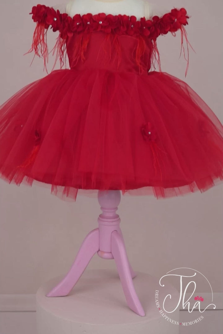 360° view of a red sleeveless designer dress that has 3D flowers with rhinestones, cap sleeve, feathers, illusion collar, satin top, and knee length skirt