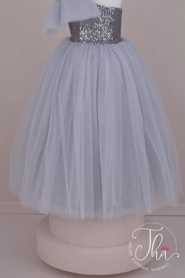 360° view of a gray sleeveless bridesmaid wedding dress that has a gray sequin top and a full gray skirt. It is decorated with a tulle bow on right shoulder