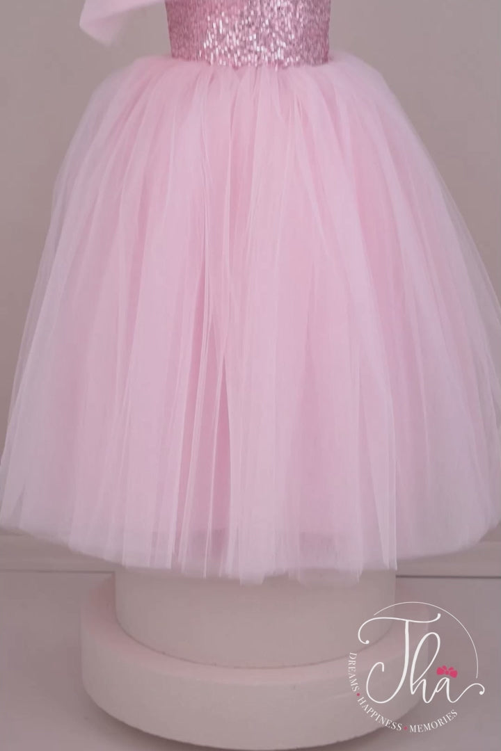 360° view of a pink sleeveless bridesmaid wedding dress that has a pink sequin top and a full pink skirt. It is decorated with a tulle bow on right shoulder