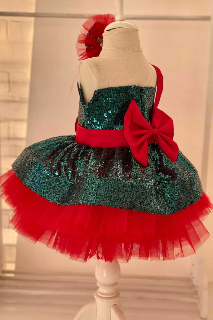 Back view of a green and red Christmas dress. The dress has a green sequin top, a knee length red skirt, red ribbon. The skirt is made of layers of red tulle