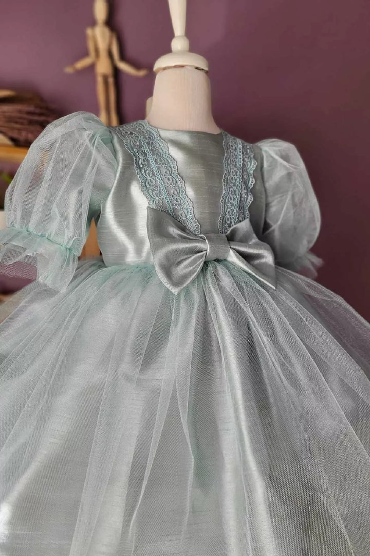 Close up view of a mint green vintage dress that has balloon arm, crystal tulle, ribbon, applique, and knee length skirt