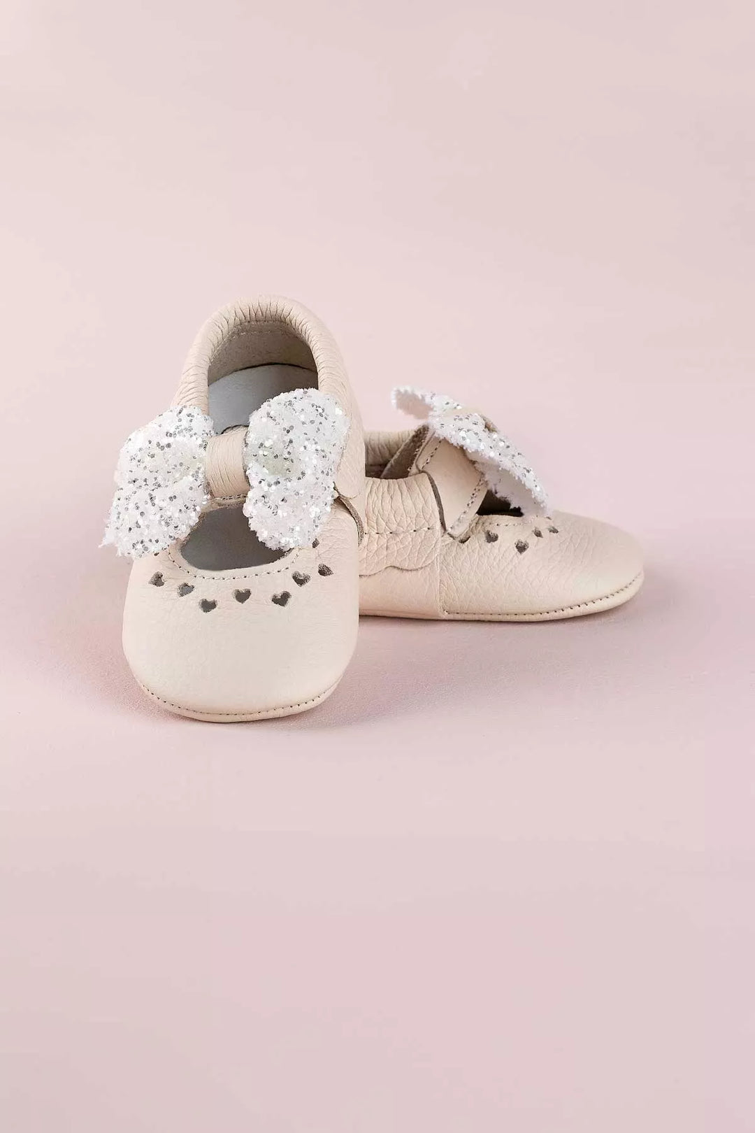 Cream baby shoes that have glitter bow tie and heart details