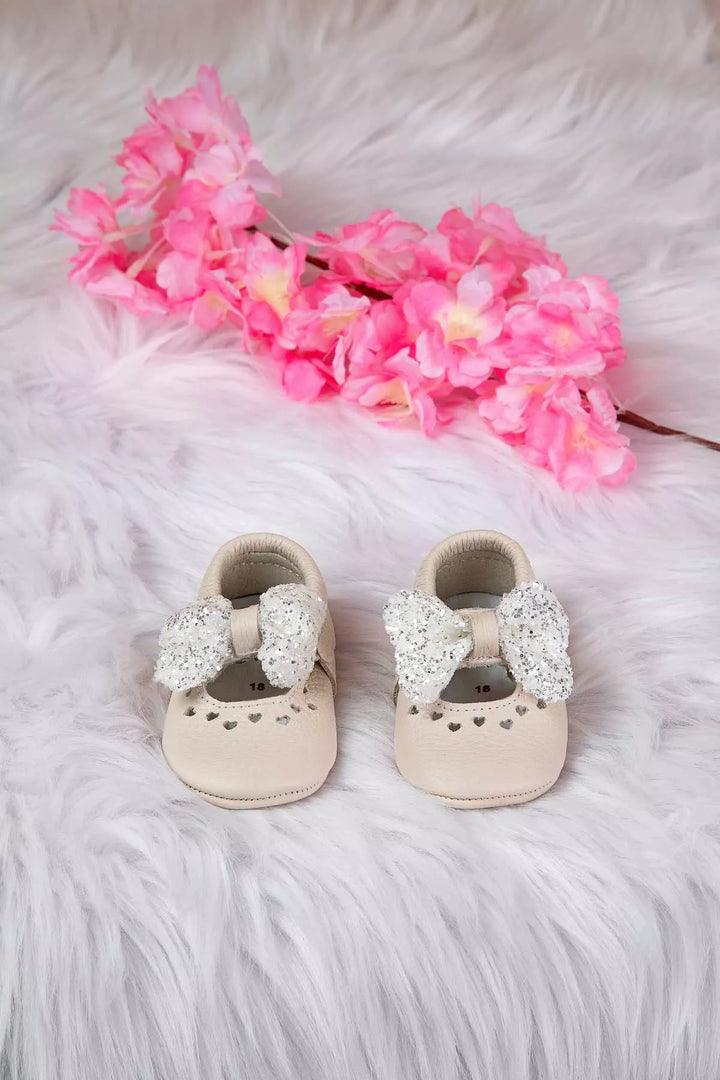 Cream baby shoes that have glitter bow tie and heart details