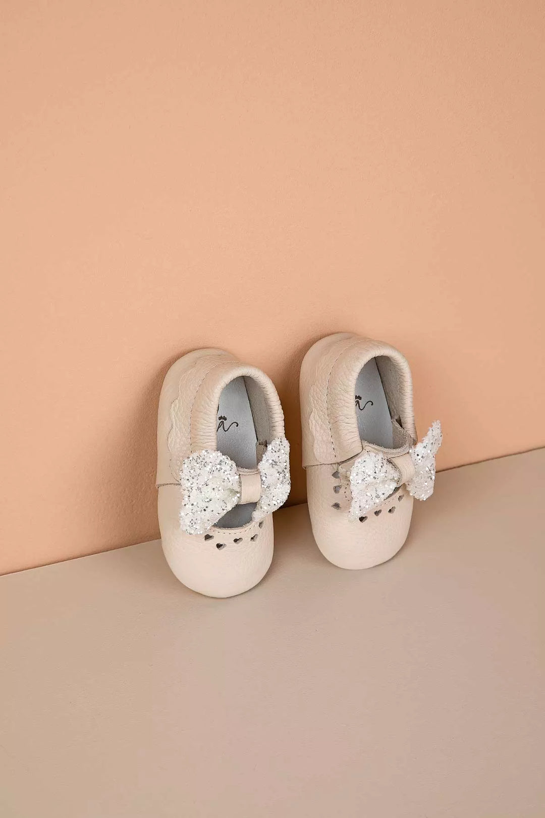 Cream baby shoes that have glitter bow tie and heart details