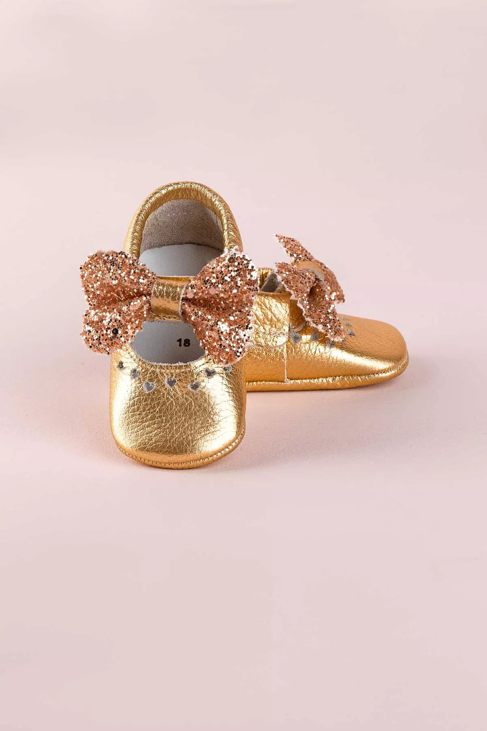 Gold baby shoes that have glitter bow tie and heart details