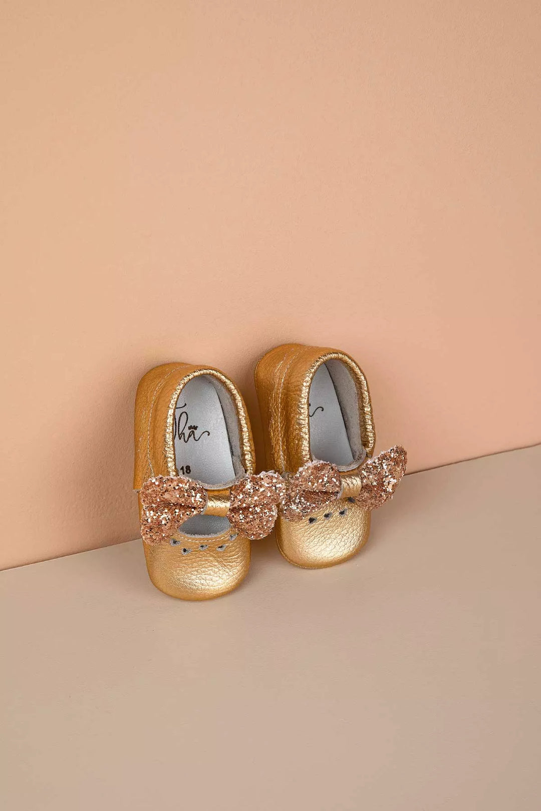 Gold baby shoes that have glitter bow tie and heart details