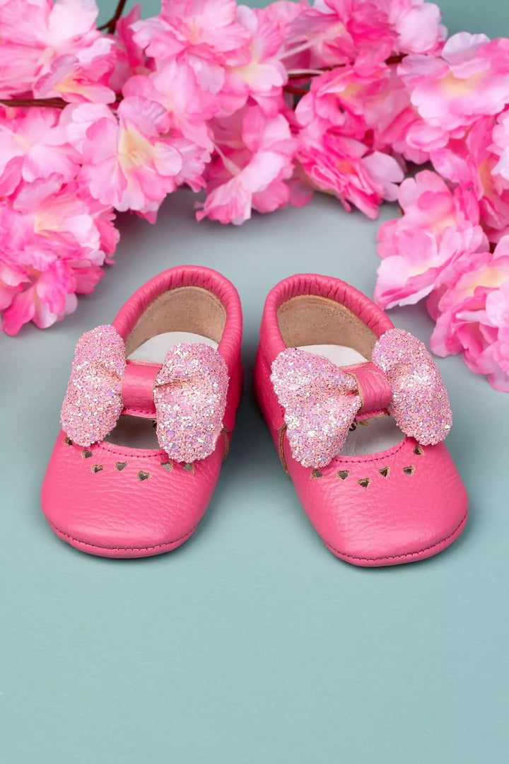 Pink baby shoes that have glitter bow tie and heart details