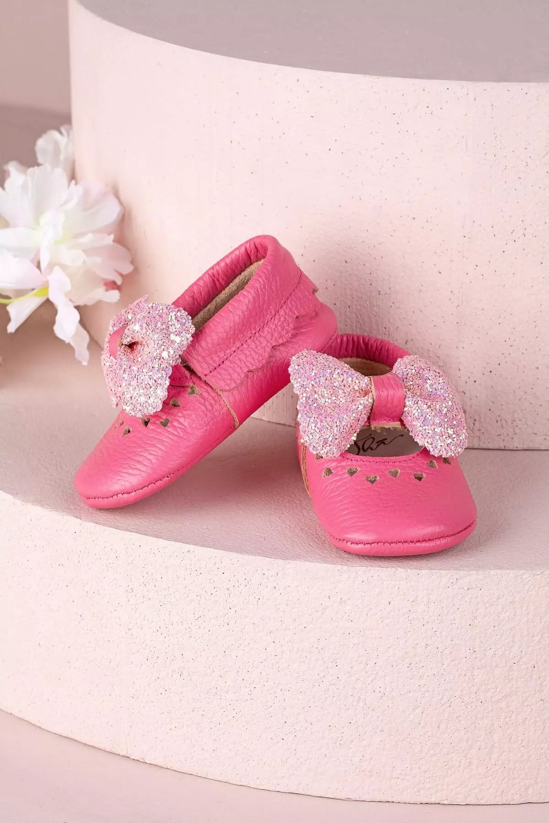 Pink baby shoes that have glitter bow tie and heart details