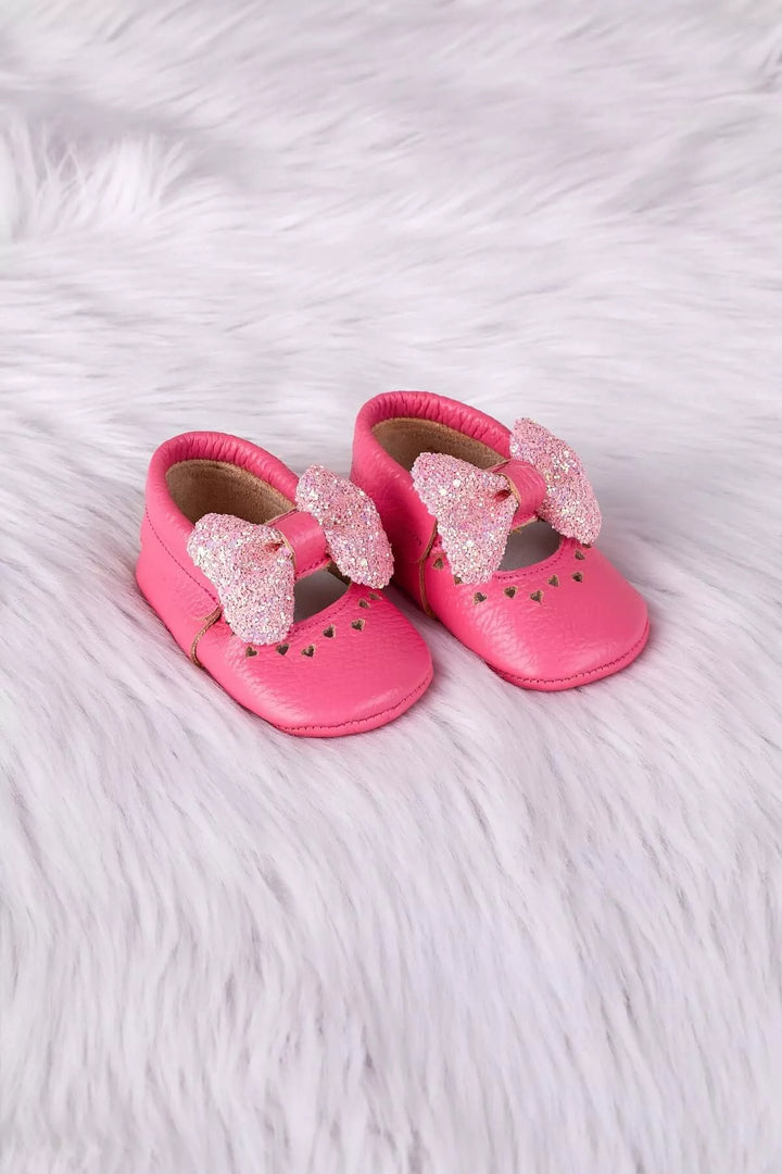 Pink baby shoes that have glitter bow tie and heart details