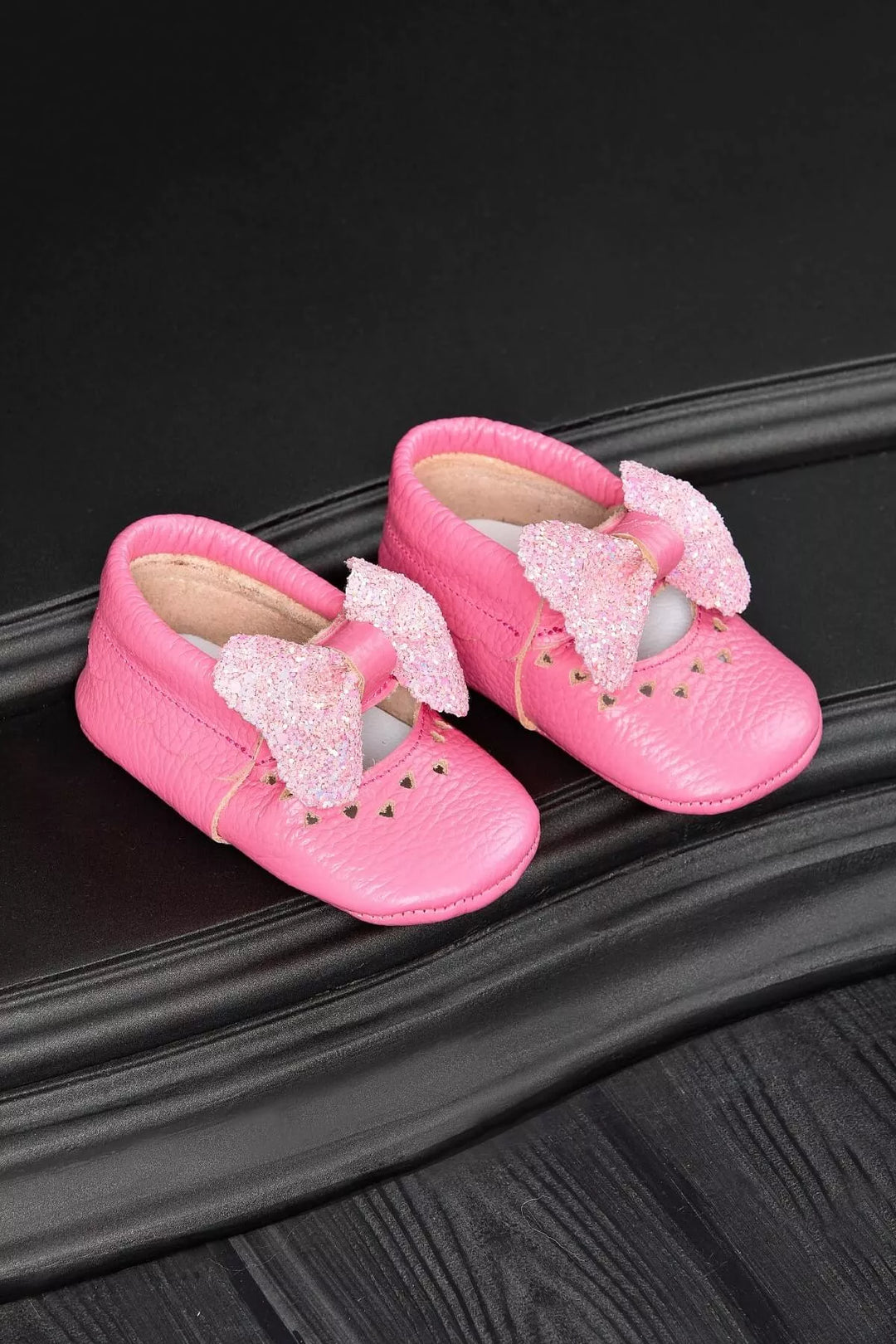 Pink baby shoes that have glitter bow tie and heart details