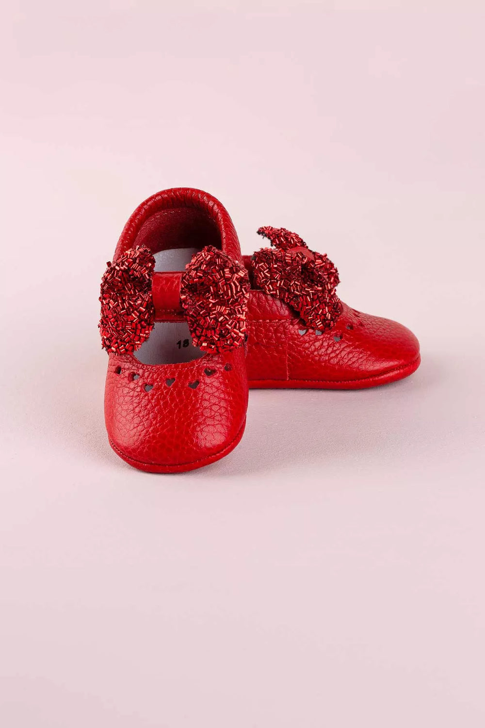 Red baby shoes that have glitter bow tie and heart details