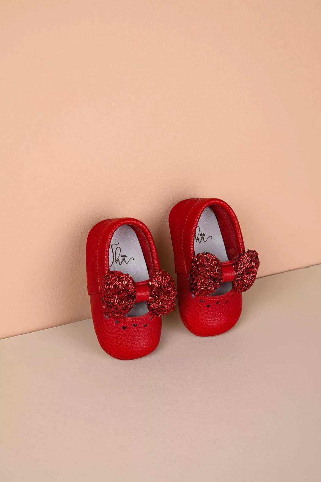 Red baby shoes that have glitter bow tie and heart details