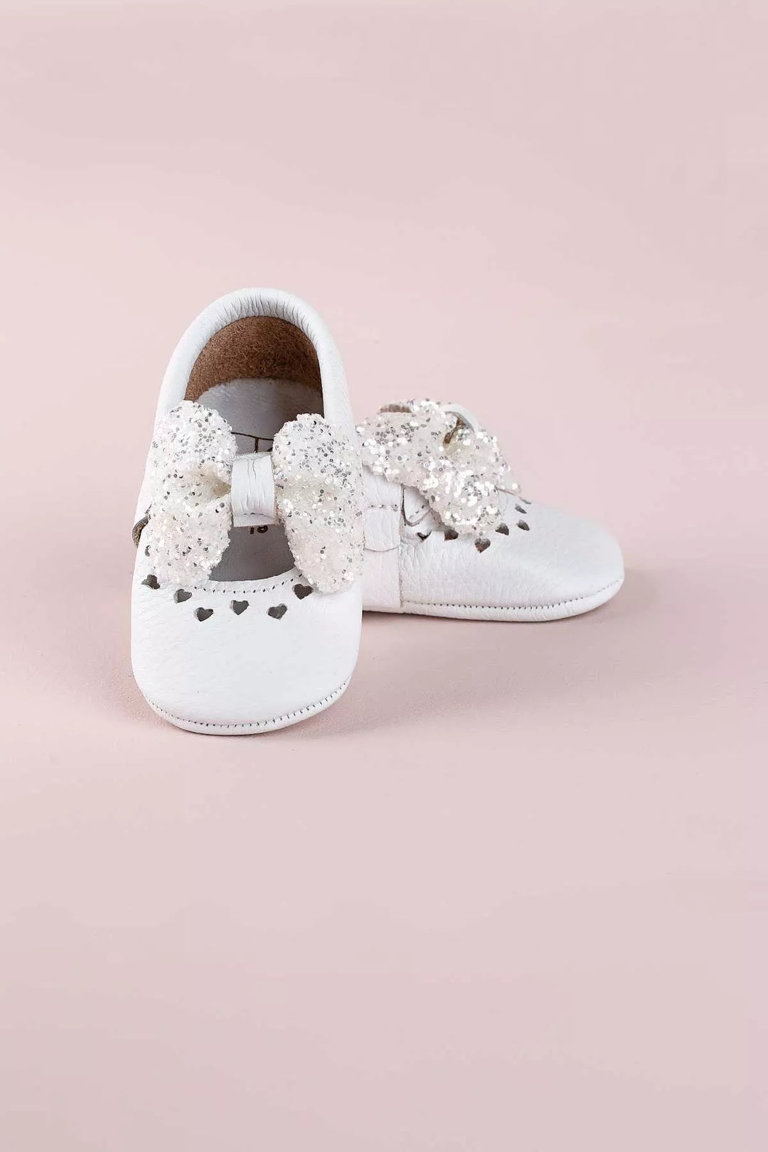 White baby shoes that have glitter bow tie and heart details