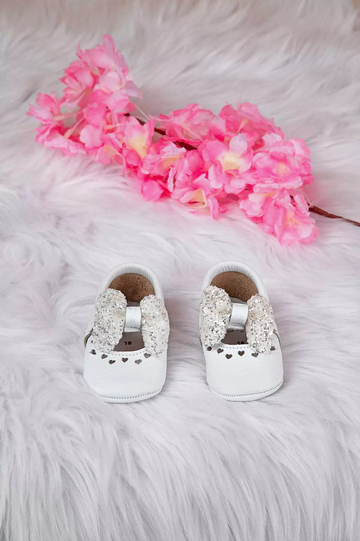 White baby shoes that have glitter bow tie and heart details