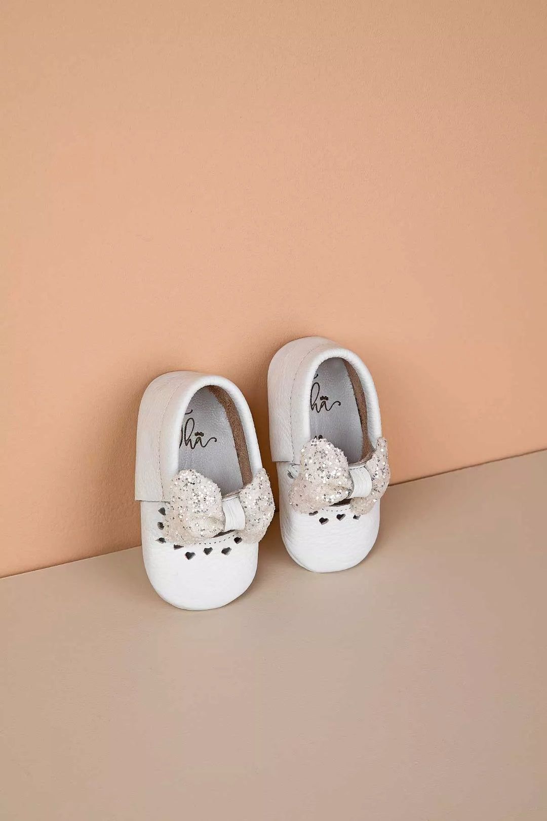 White baby shoes that have glitter bow tie and heart details