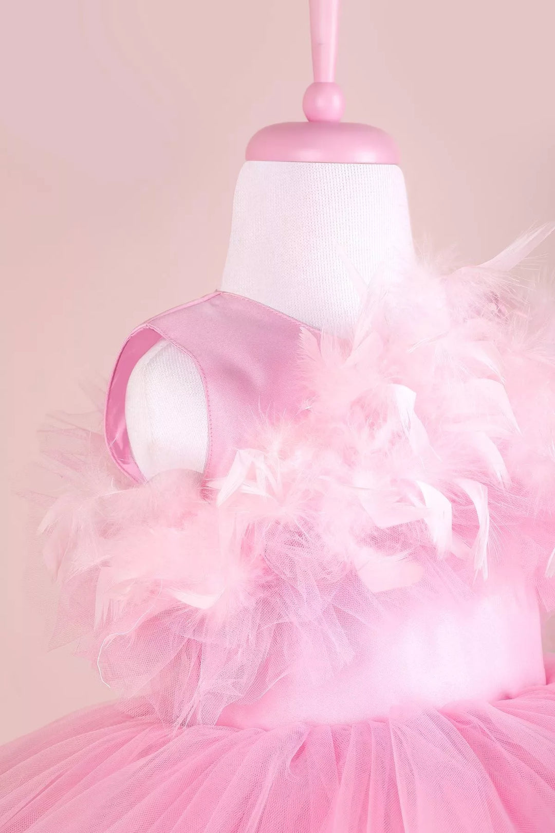 Close up view of a pink princess wedding dress. The dress has satin top and feathers on chest