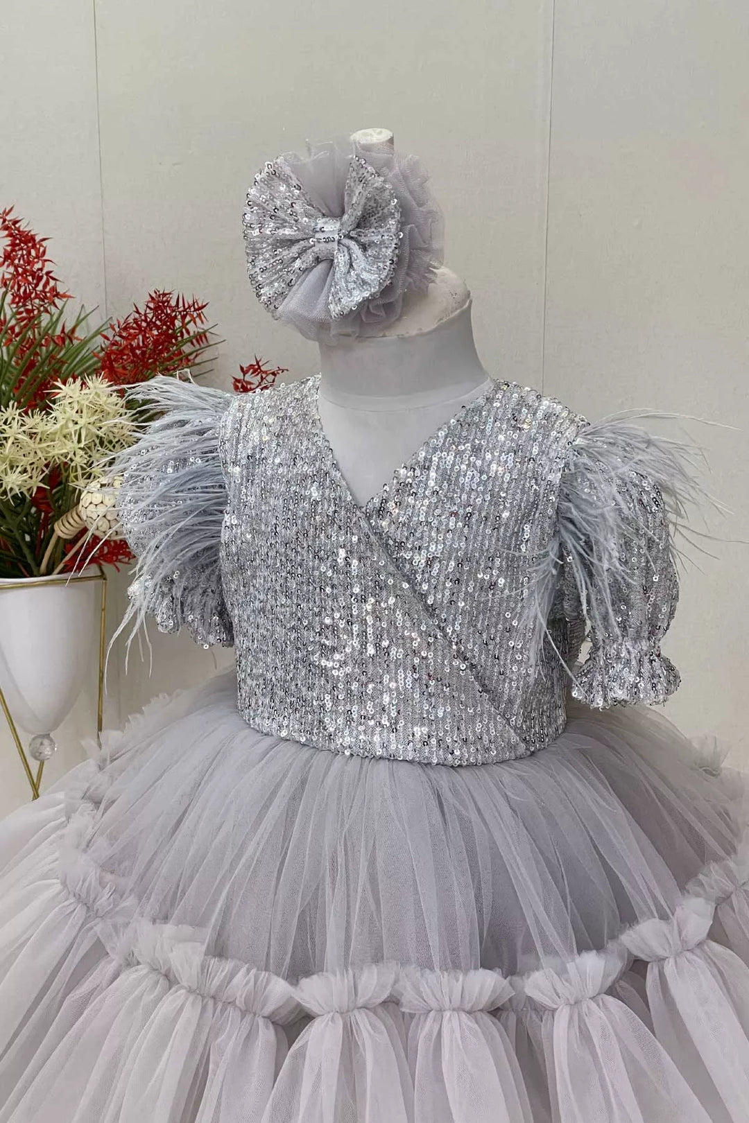 Close up view of a gray girl dress that has sequins, half sleeve, feathers, V-neck, and puffy skirt