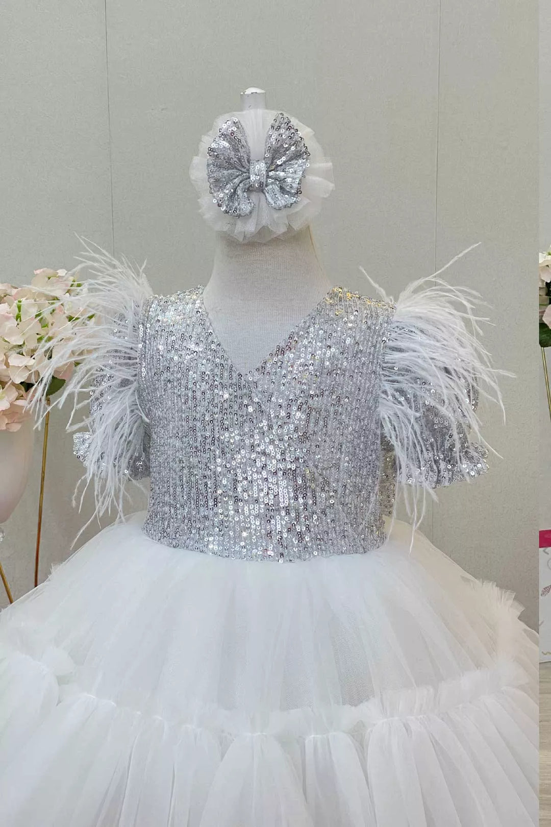 Close up view of a white girl dress that has sequins, half sleeve, feathers, V-neck, and puffy skirt