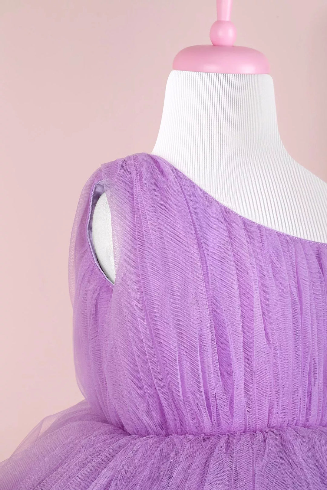 Close up view of a lilac one shoulder open sleeveless prom dress that has knee length shirred skirt