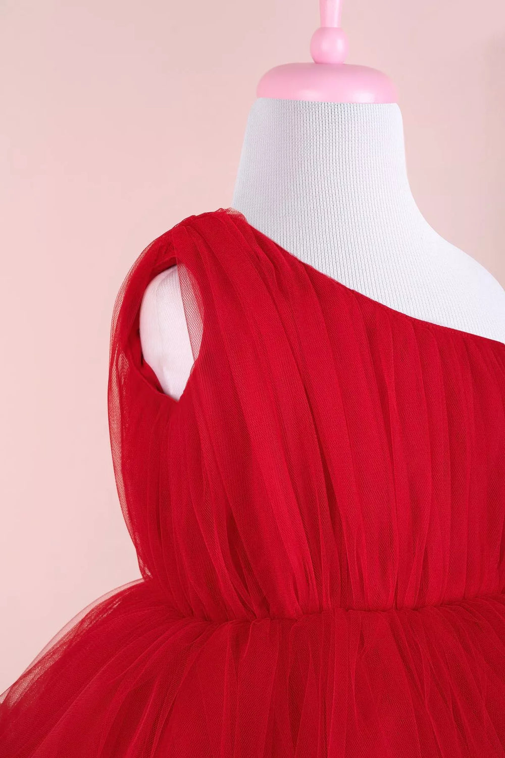 Close up view of a red one shoulder open sleeveless Christmas dress that has knee length shirred skirt