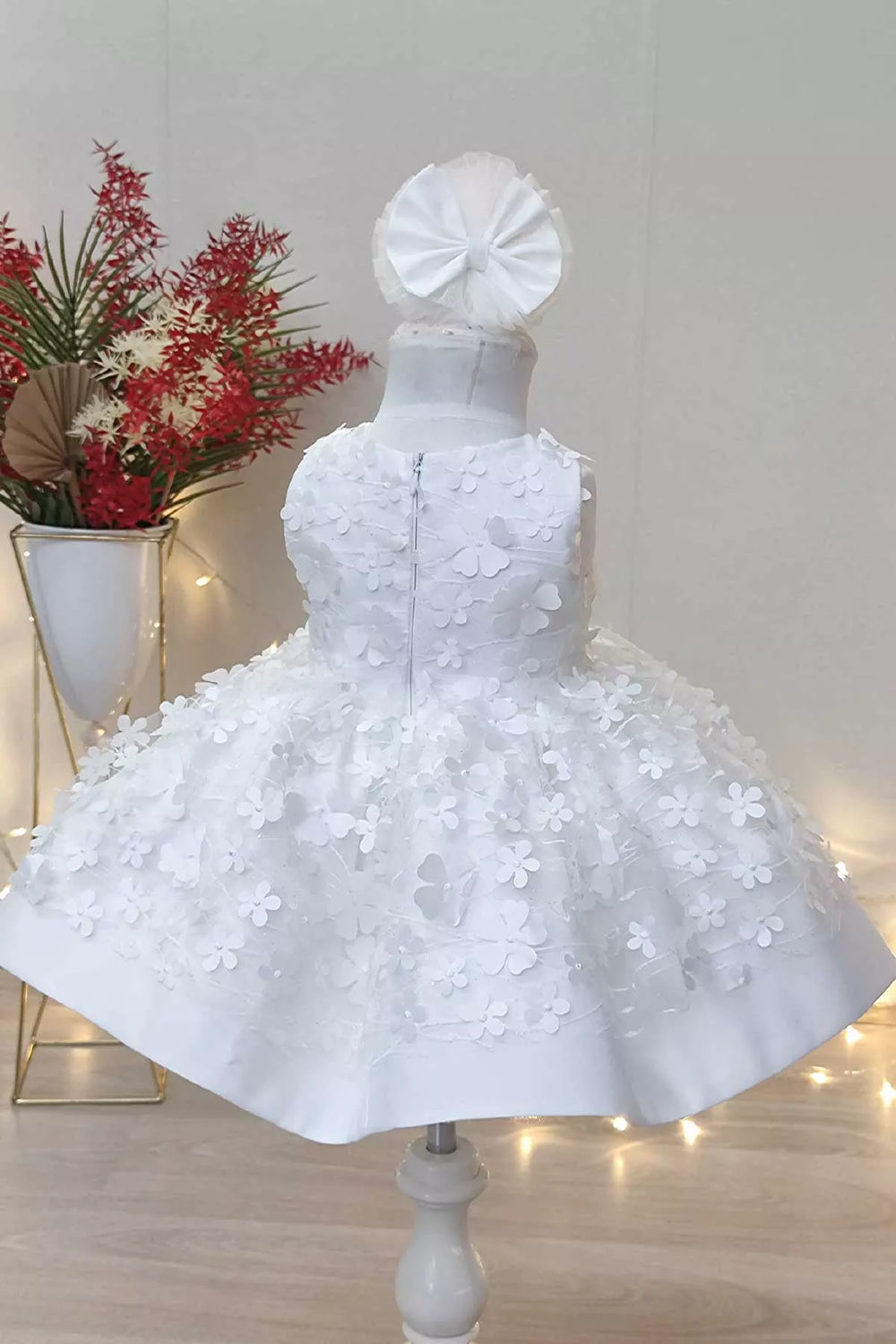 Back view of a white snow themed floral sleeveless dress that has 3D flowers and low skirt